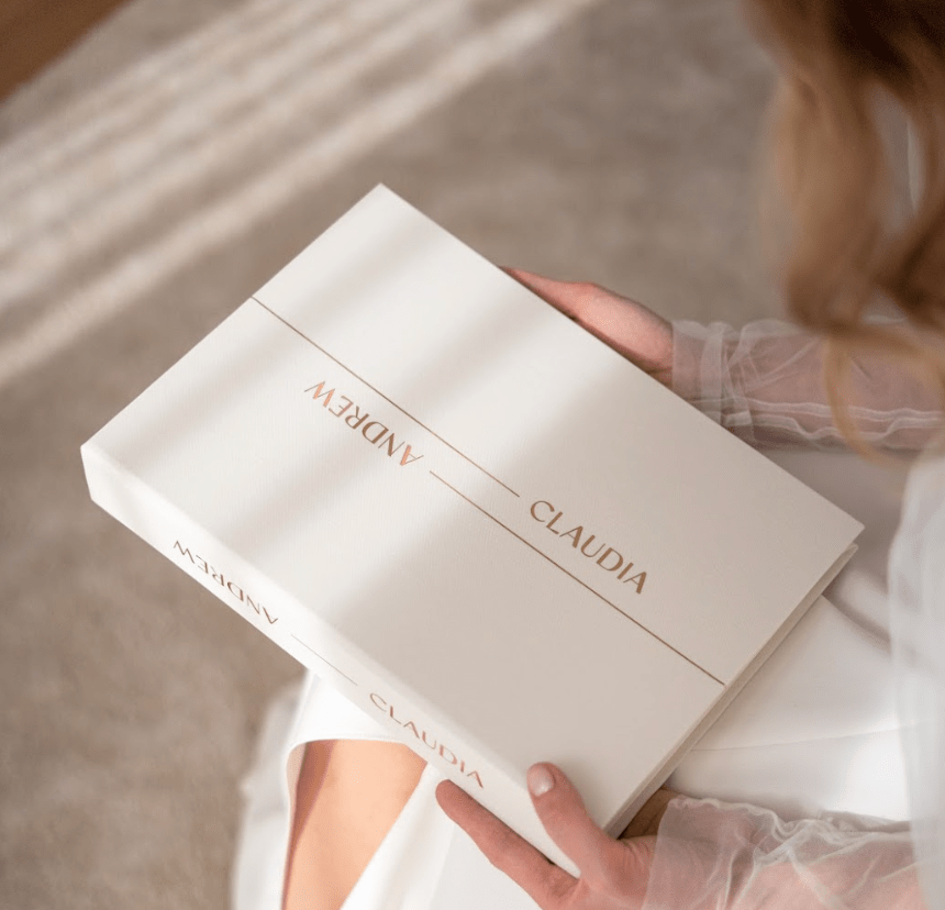 Person holding a white book with gold text on a neutral background